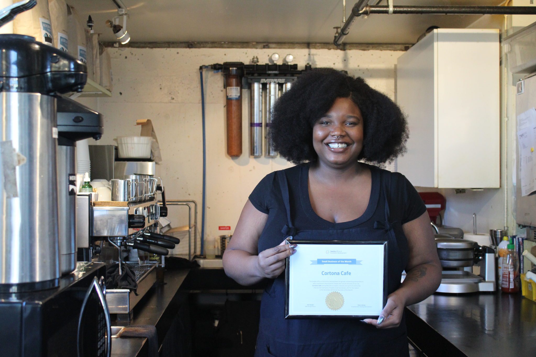 Cortona Cafe owner Isolynn Dean holding a Small Business of the Month certificate.