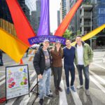 Mayor Katie Wilson, Director Beto Yarce, and two other people pose for a photo in front of the South Lake Union farmers market sign.